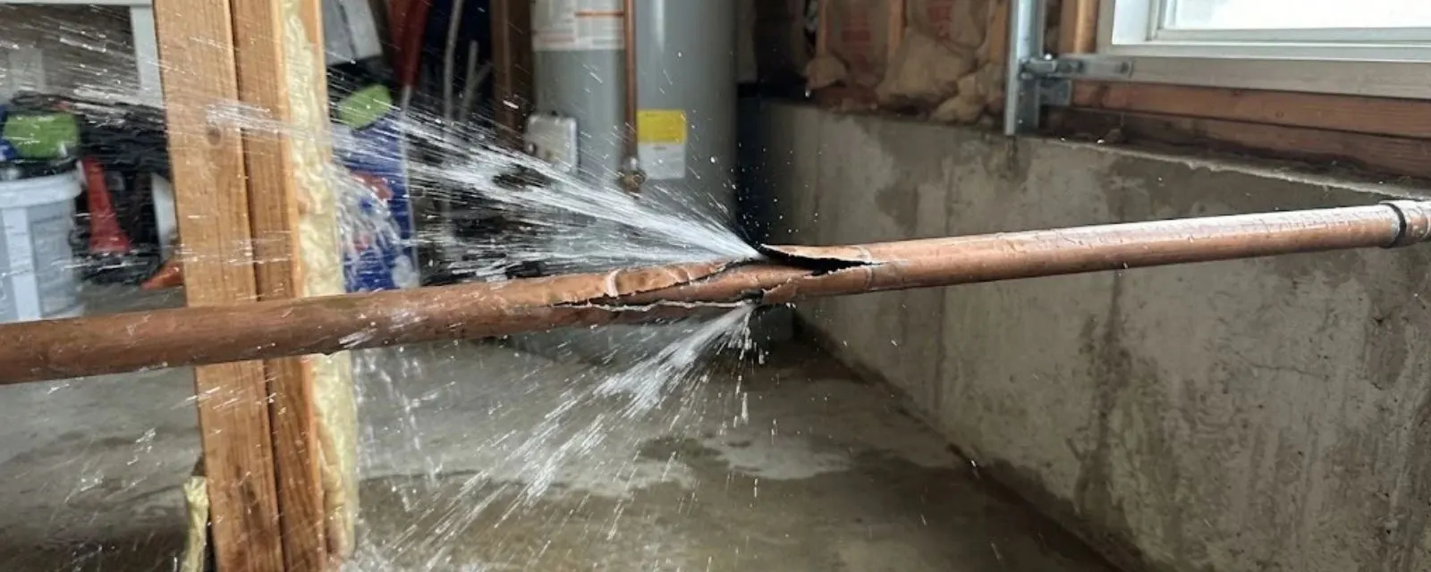 Burst pipe repair: burst copper pipe spraying water in a basement next to a water heater
