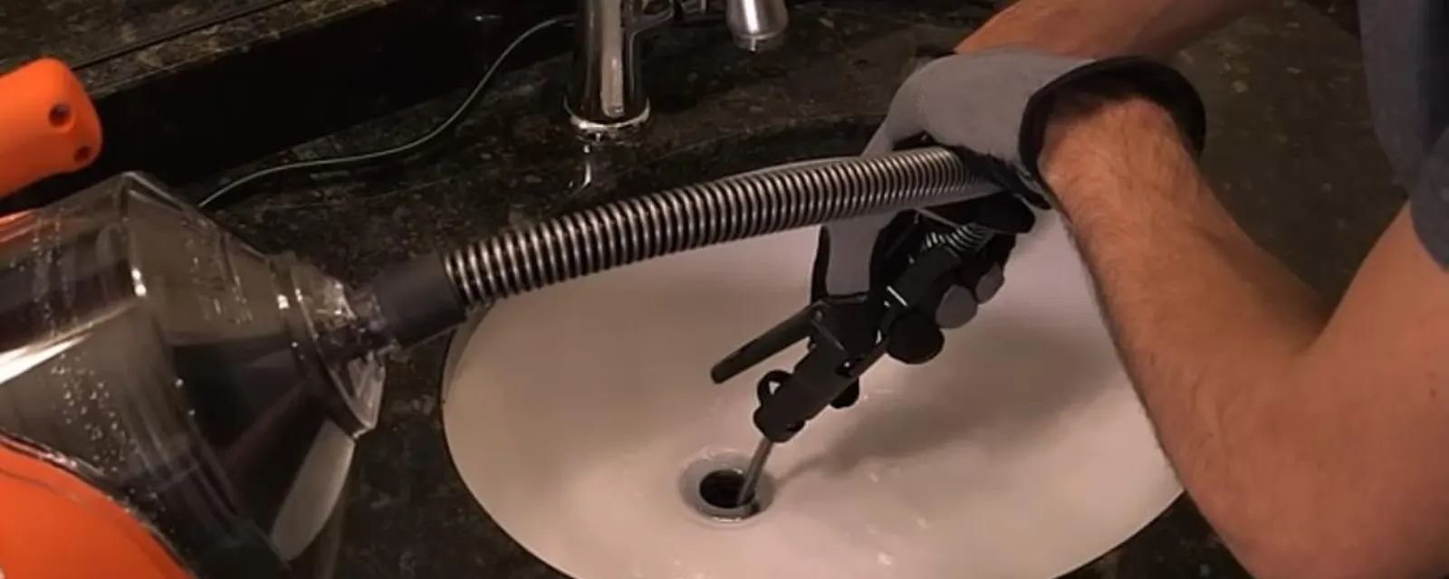 Drain cleaning: plumber feeding a drain snake into a kitchen sink drain