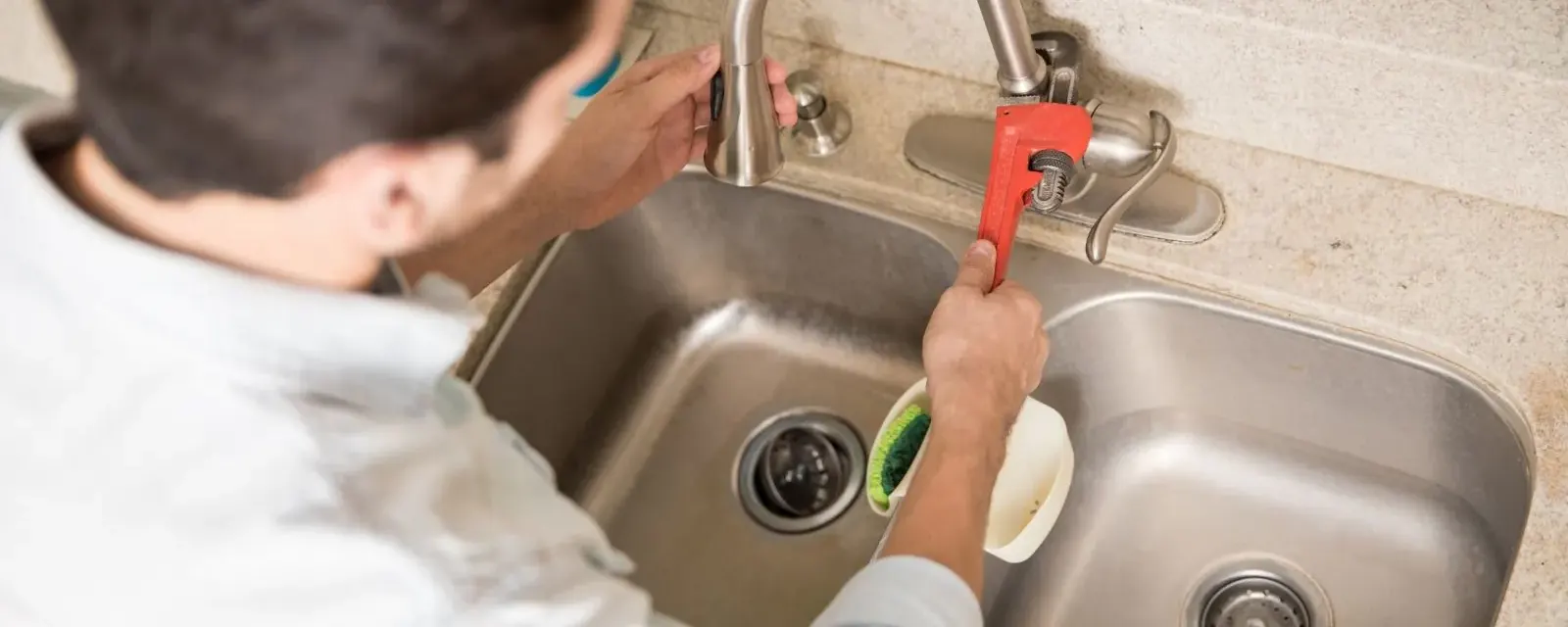Faucet repair: person using a pipe wrench on a kitchen sink faucet